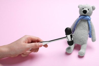 Woman pretending to test teddy bear's reflexes with hammer on pink background, closeup. Nervous system diagnostic