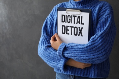 Photo of Woman holding clipboard with phrase DIGITAL DETOX on grey background, closeup. Space for text