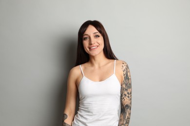 Beautiful woman with tattoos on arms against grey background