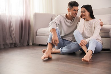 Happy couple sitting on warm floor in living room, space for text. Heating system