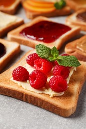 Photo of Tasty toast with butter, raspberry and mint on light grey table, closeup