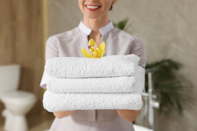 Chambermaid holding fresh towels with flower in hotel bathroom, closeup