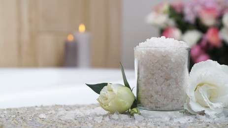 Glass with bath salt and beautiful flowers on wicker mat in bathroom, closeup. Space for text