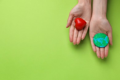 Woman holding model of planet and red heart on green background, top view with space for text. Earth Day