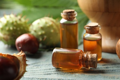 Chestnuts and bottles of essential oil on blue wooden table, closeup