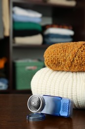 Photo of Fabric shaver and knitted clothes on wooden table indoors