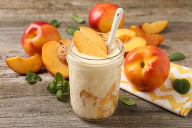Tasty peach yogurt with pieces of fruit and spoon in glass jar on wooden table