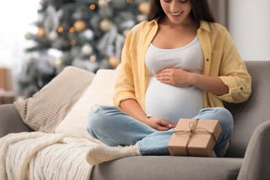 Happy pregnant woman with gift box in living room decorated for Christmas, closeup. Expecting baby