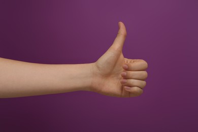 Woman showing thumb up on purple background, closeup
