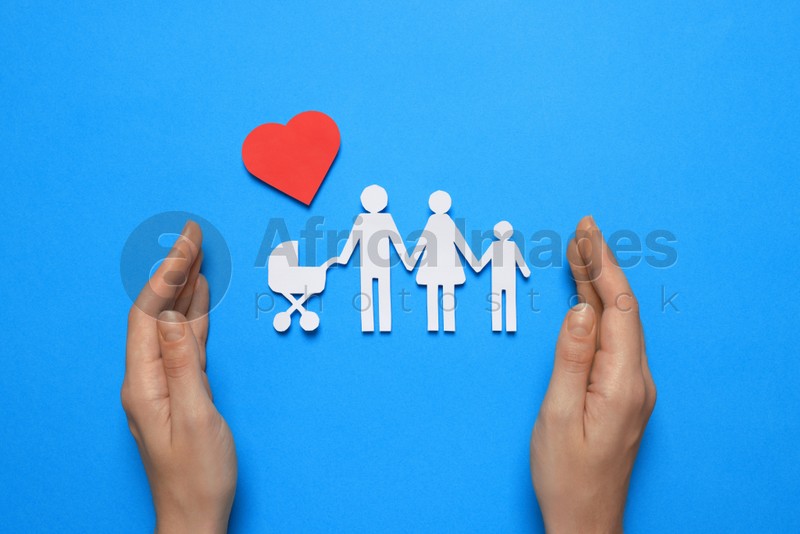 Photo of Woman protecting paper family cutout on light blue background, top view. Insurance concept