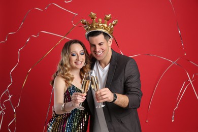 Happy couple with champagne and falling down serpentines on red background