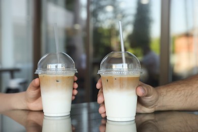 Photo of Man and woman with plastic takeaway cups of delicious iced coffee at table in outdoor cafe, closeup