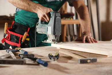 Professional carpenter working with jigsaw at workbench, closeup
