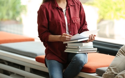Young woman with books sitting near window in library, closeup