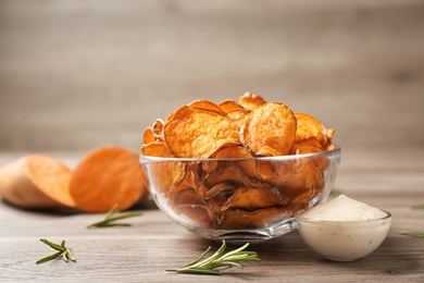 Delicious sweet potato chips in bowl, rosemary and sauce on table