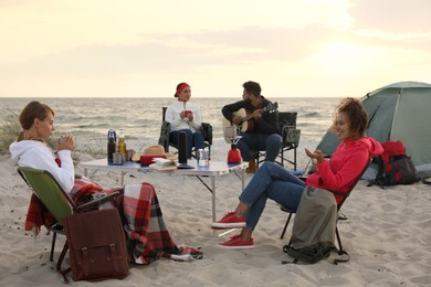Friends resting near camping tent on sandy beach