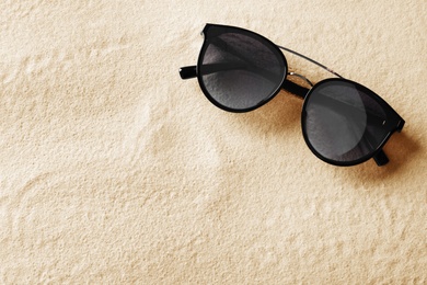 Stylish sunglasses on white sand, top view. Space for text