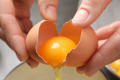 Woman separating egg yolk from white over bowl, closeup