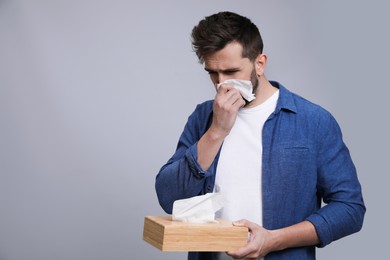 Man blowing nose on grey background, space for text. Cold symptoms