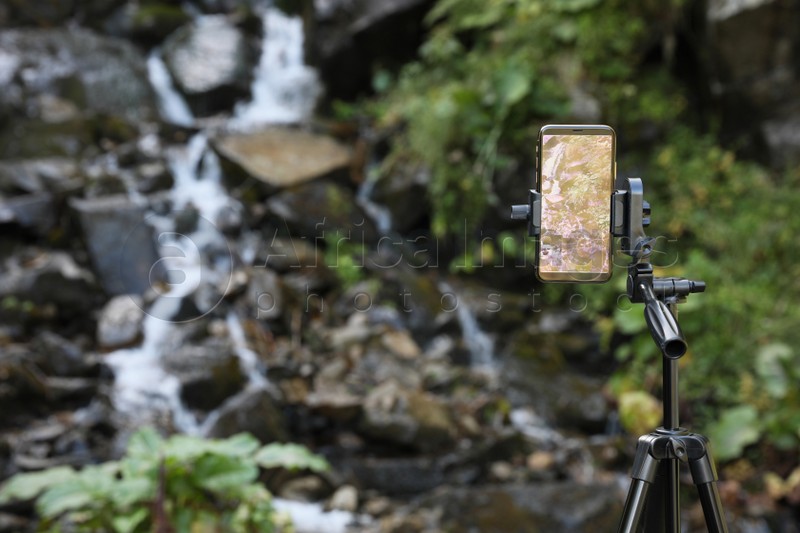 Photo of Taking video of mountain stream with modern phone on tripod outdoors