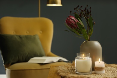 Photo of Vase with beautiful protea flowers and burning candles on wooden table indoors, space for text. Interior elements
