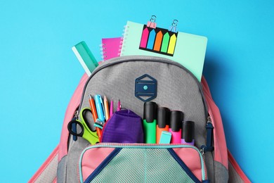 Backpack with school stationery on light blue background, top view