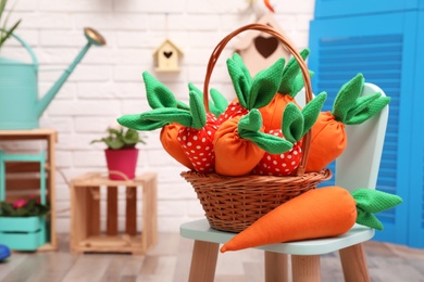 Wicker basket with cute toy carrots on chair indoors, space for text