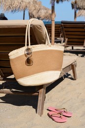 Photo of Straw bag with sunglasses on wooden sunbed near sea. Beach accessories