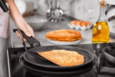 Woman cooking delicious thin pancakes on induction stove, closeup