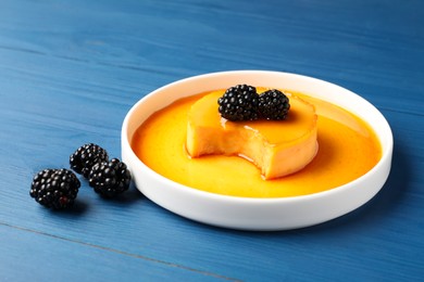 Photo of Delicious pudding with caramel and blackberries on blue wooden table