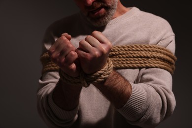 Photo of Victim tied with rope on dark background, closeup. Hostage taking