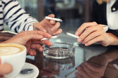 Women holding cigarettes over glass ashtray at table, closeup