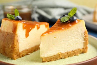 Photo of Pieces of delicious caramel cheesecake with blueberry and mint on table, closeup