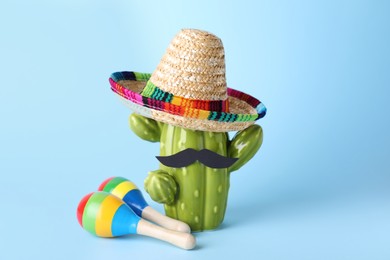 Photo of Colorful maracas, toy cactus with sombrero hat and mustache on light blue background. Musical instrument
