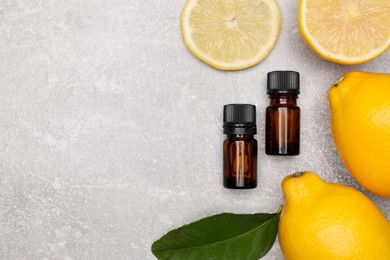 Bottles of essential oil with lemons and leaf on grey table, flat lay. Space for text