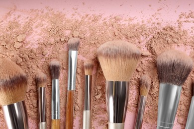 Makeup brushes and scattered face powder on pink background, flat  lay