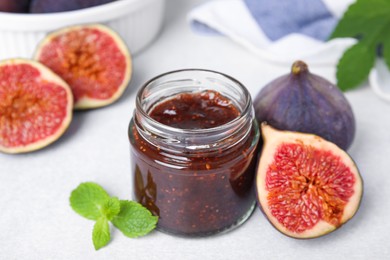 Photo of Glass jar of tasty sweet fig jam and fruits on light table, closeup