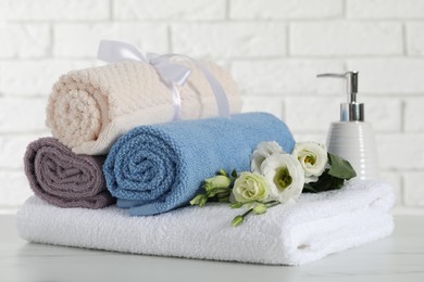 Photo of Rolled and folded towels with flowers on white table, closeup