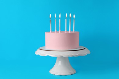 Birthday cake with burning candles on light blue background