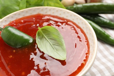 Spicy chili sauce with basil on table, closeup