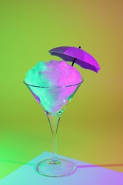Photo of Beautiful martini glass with cotton candy and umbrella on color background