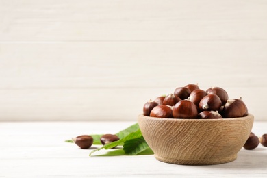 Fresh sweet edible chestnuts in bowl on white wooden table. Space for text