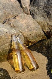 Bottles of cold beer near rock on sandy beach