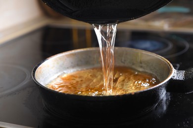 Photo of Pouring used cooking oil onto frying pan on stove