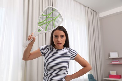 Photo of Young woman with electric fly swatter indoors. Insect killer