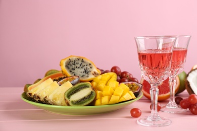 Delicious exotic fruits and glasses of wine on pink wooden table