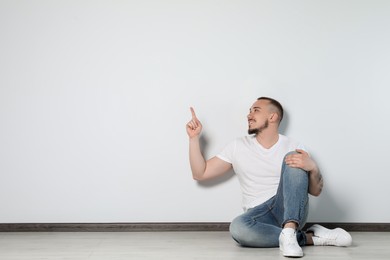 Photo of Handsome young man sitting on floor near white wall indoors, space for text