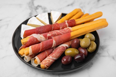 Photo of Plate of delicious grissini sticks with prosciutto, cheese and olives on white marble table