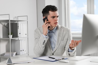 Confused businessman talking on phone while working in office