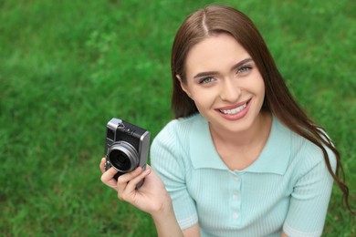 Young woman with camera on green grass outdoors, space for text. Interesting hobby